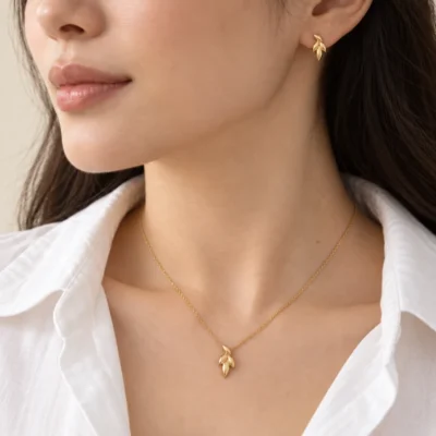 مدال و گوشواره طلا طرح خوشه روی مدل با لباس سفید؛ زنجیر صرفاً نمایشی است