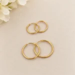 دو جفت گوشواره طلا حلقه‌ای ساده در اندازه کوچک و متوسط روی پارچه بژ